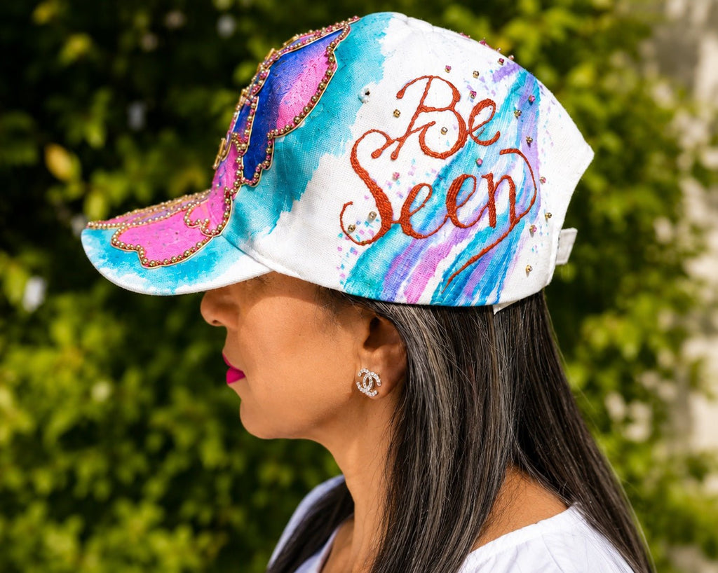 Woman wearing a colorful visor with 'Be Seen' text against a green leafy background